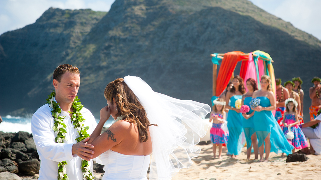 Bride and groom on the beach with the bridal party in turquoise behind them